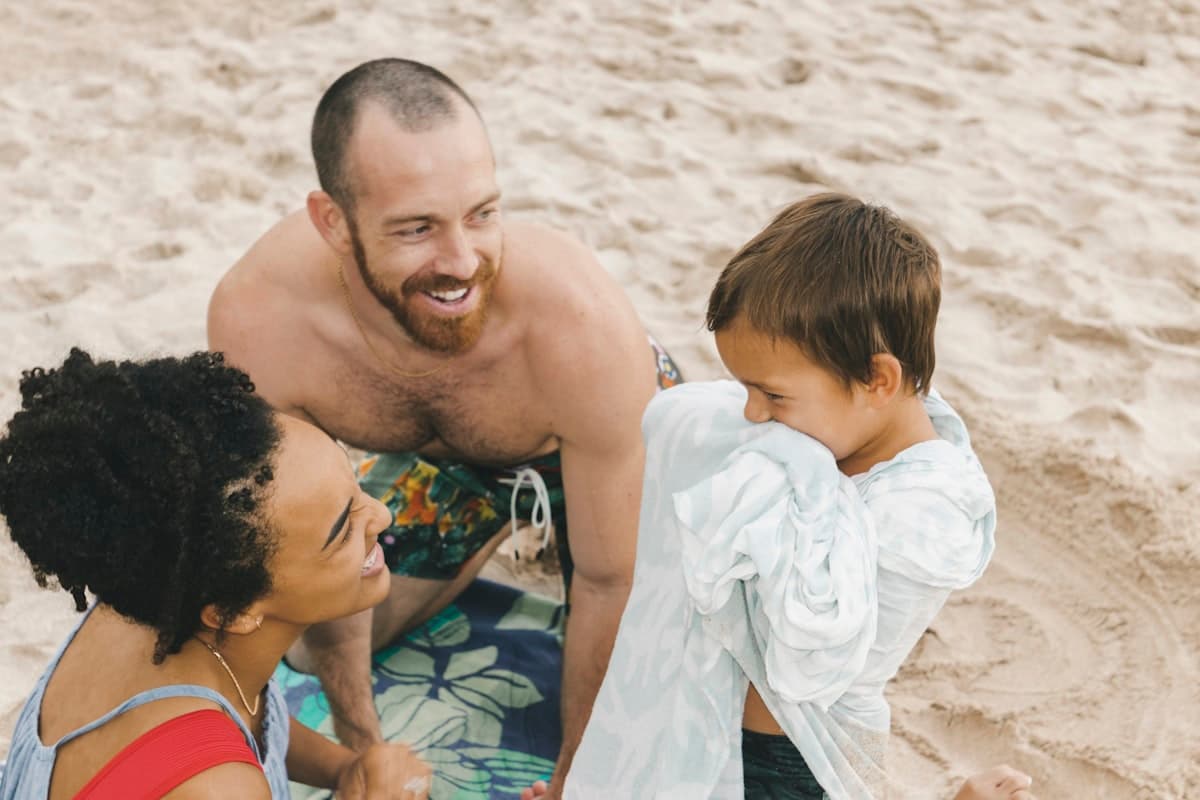 Parents laughing together while wrapping their son in a towel on the beach