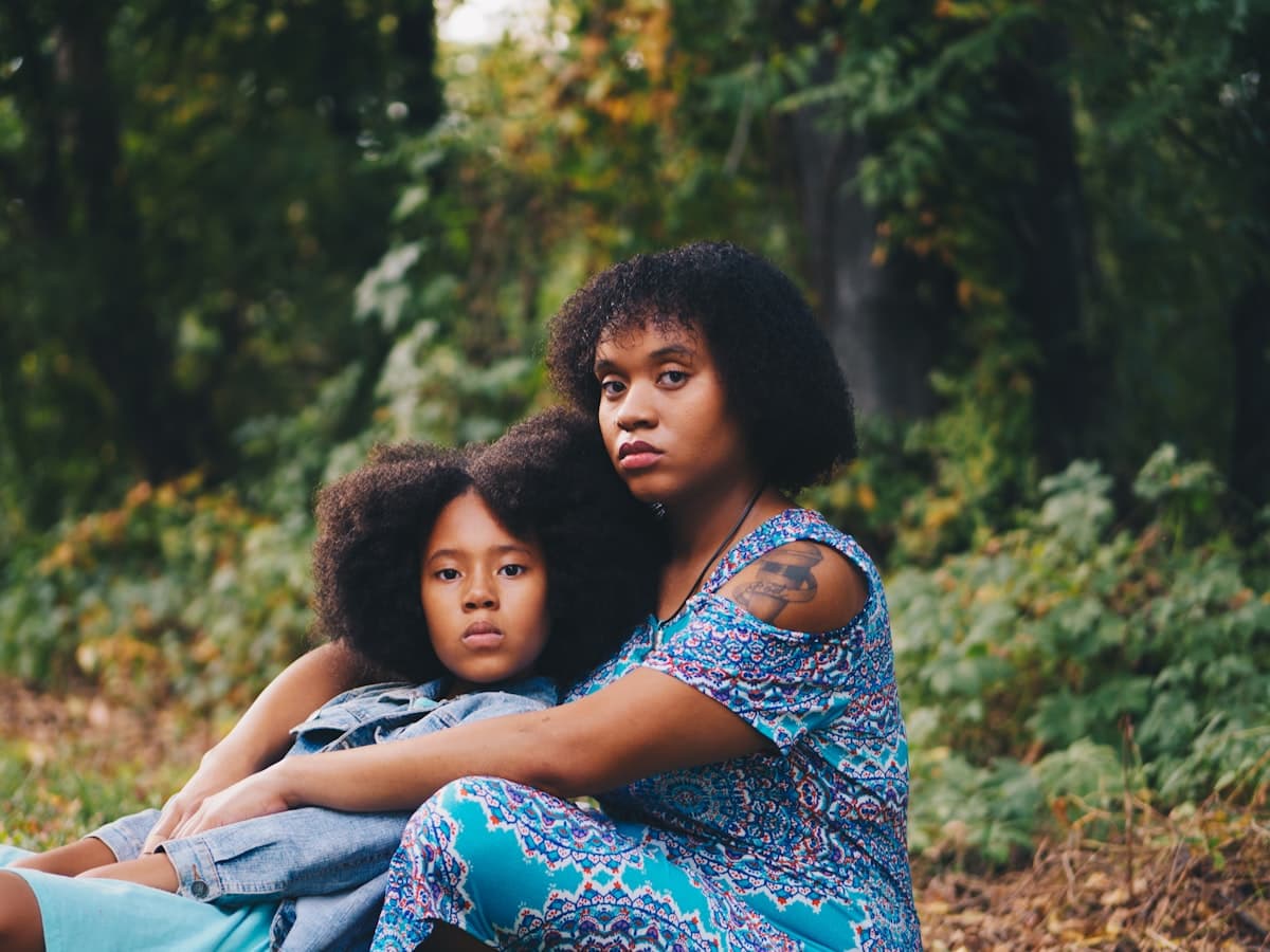 A mother and daughter sitting together outdoors among the trees