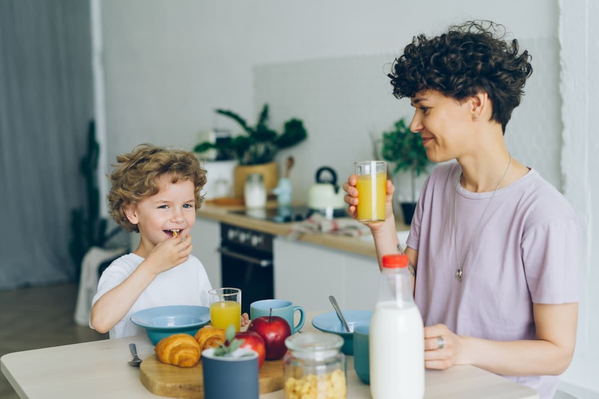 A parent and child laughing over breakfast in a bright kitchen